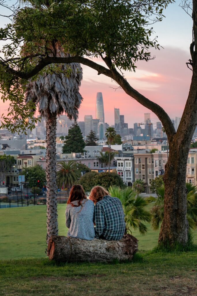 A couple sitting on a log at sunset at Dolores Park overlooking San Francisco skyline.