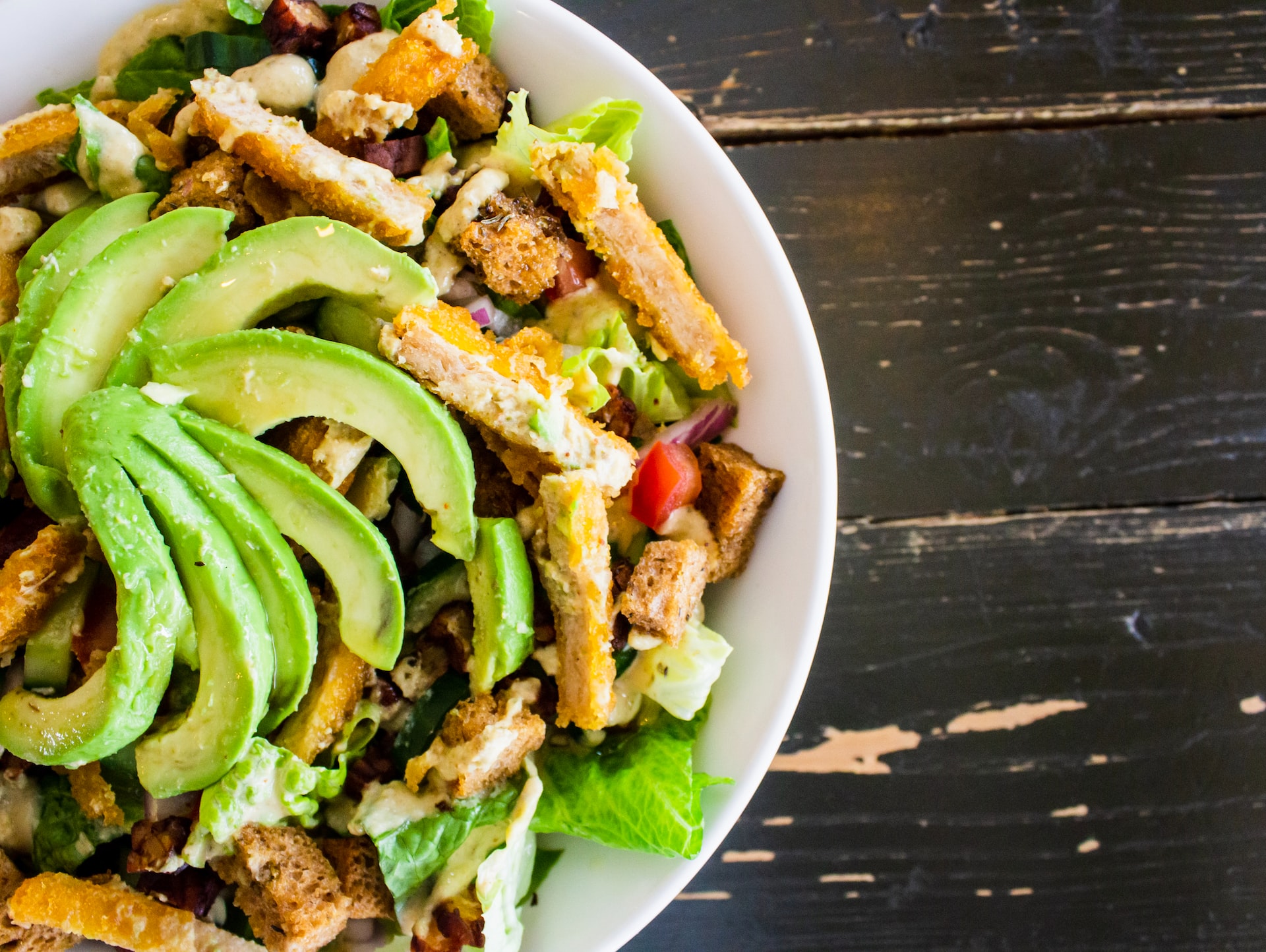 Close up of a salad with chicken, avocado, peppers, and croutons.