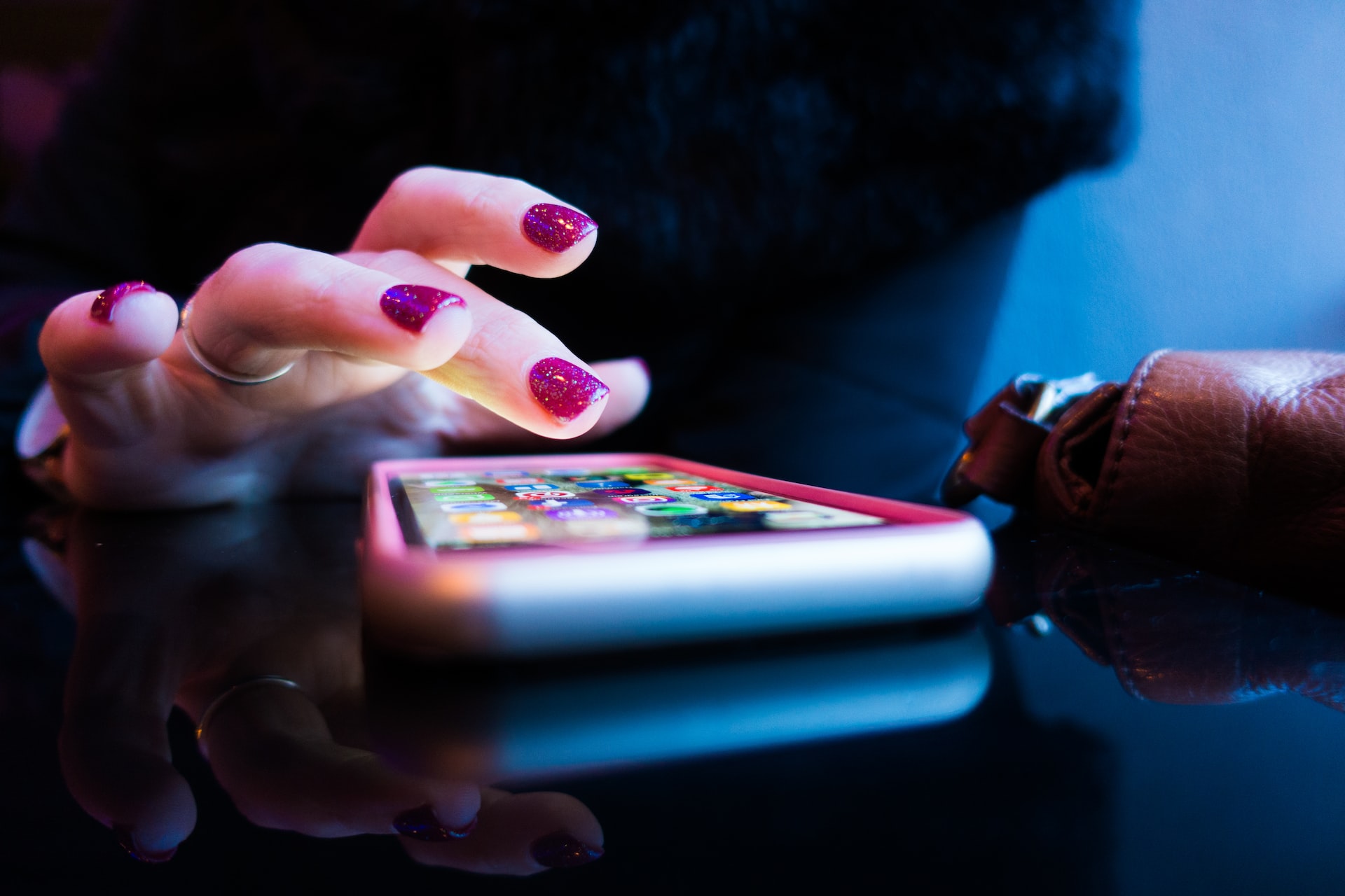 Woman with sparkly magenta nail polish taps on her smartphone.