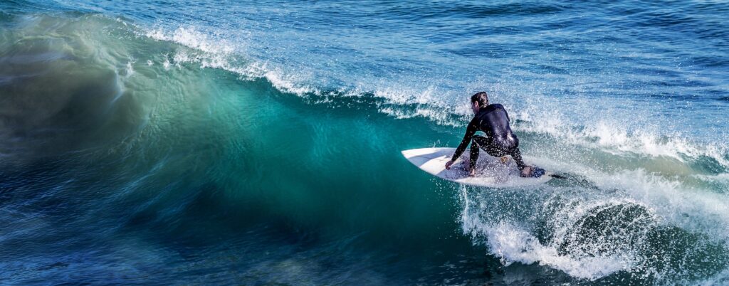 A surfer in a black wetsuit catching a wave.