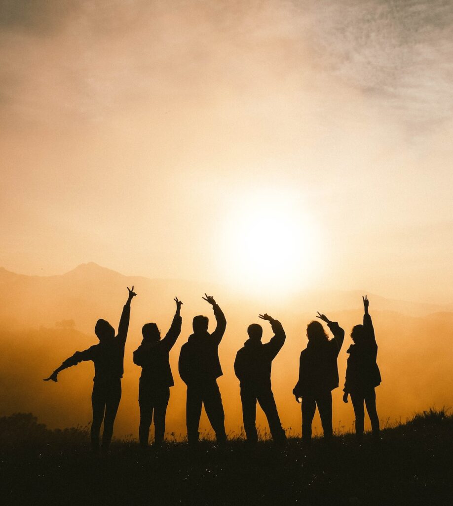 Silhouettes of people with hands above their heads in front of a sunset.